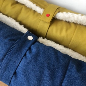 May include: Two long, rectangular cushions with white sherpa trim. One cushion is a dark blue denim fabric with a silver button. The other cushion is a mustard yellow fabric with a red button and a strap.