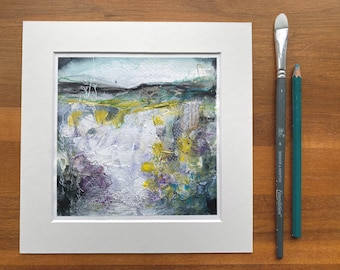 May include: Abstract landscape painting in a white mount. The artwork features a textured, mixed-media style with colours of white, yellow, purple, and green. A paintbrush and a pencil are placed to the right of the artwork.