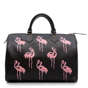 May include: Black leather handbag with pink flamingo print. The bag has a top handle and a zipper closure.
