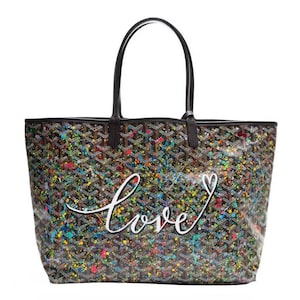 May include: A tote bag with a black and brown geometric pattern, overlaid with colorful paint splatters. The word "love" is written in white script across the front, with a heart symbol. The bag has black handles.