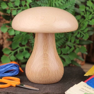 May include: A wooden mushroom-shaped needle minder with a light brown finish. The needle minder is a small, decorative object used to hold needles while sewing.