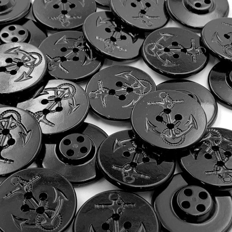 Puede incluir: Una colecci&oacute;n de botones de pl&aacute;stico negro con un dise&ntilde;o de ancla. Los botones tienen cuatro agujeros y son brillantes.