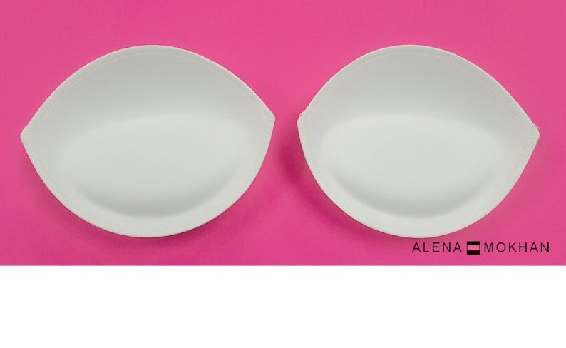 Puede incluir: Dos insertos de sujetador blancos, con forma de l&aacute;grima, sobre un fondo rosa.