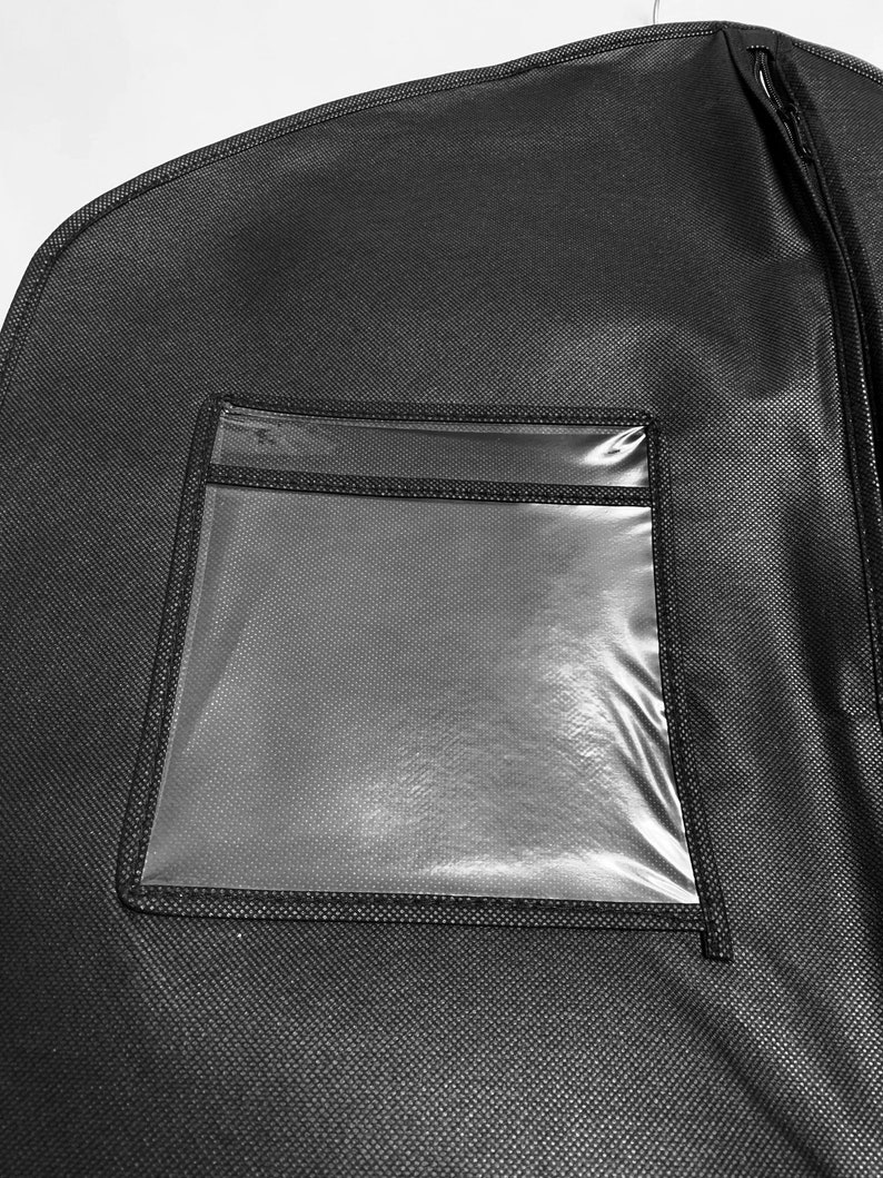 Pu&ograve; includere: Custodia per abiti nera con una finestra rettangolare trasparente. La borsa ha una chiusura a cerniera ed &egrave; appesa a un gancio di metallo. Il materiale ha un aspetto strutturato.
