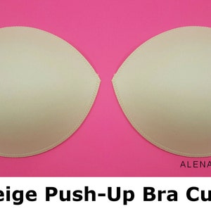 Puede incluir: Dos copas de sujetador push-up beige sobre un fondo rosa. ALENA MOKHAN est&aacute; escrito en texto negro en la parte inferior de la imagen.