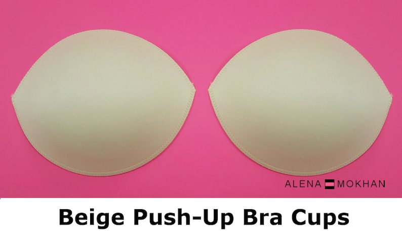 Puede incluir: Dos copas de sujetador push-up beige sobre un fondo rosa. ALENA MOKHAN est&aacute; escrito en texto negro en la parte inferior de la imagen.