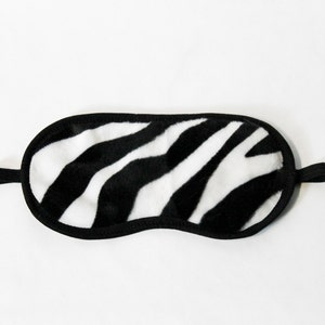 Puede incluir: Una máscara para dormir de estampado de cebra en blanco y negro con una banda elástica negra.