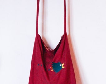 Puede incluir: Una bolsa de mano roja con un diseño de pájaro colgada de un gancho blanco.