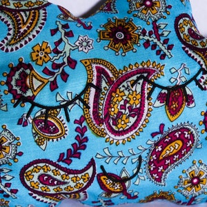 Peut inclure: Un coussin en forme d'étoile avec un motif cachemire bleu clair. Le motif comprend des motifs floraux et cachemire jaunes, bordeaux et blancs. Des cils noirs cousus sont présents sur le coussin.