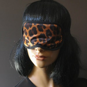 Puede incluir: Una máscara de dormir negra con estampado de leopardo.