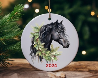 May include: A round white ceramic ornament featuring a black horse head illustration adorned with green pine branches and holly leaves. The year 2024 is printed in red at the bottom. The ornament hangs from a thin silver string.