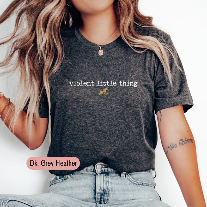 Puede incluir: Camiseta gris oscuro jaspeado con el texto blanco "violent little thing" y un peque&ntilde;o gr&aacute;fico de perro dorado. La esquina inferior izquierda de la imagen muestra el texto "Dk. Grey Heather".