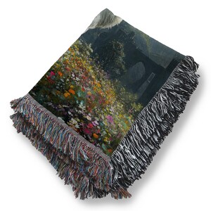 May include: Woven throw blanket featuring a landscape painting with colorful flowers and a dark background. The blanket has a fringed edge with a mix of colors and black and white. The artwork depicts a natural scene.