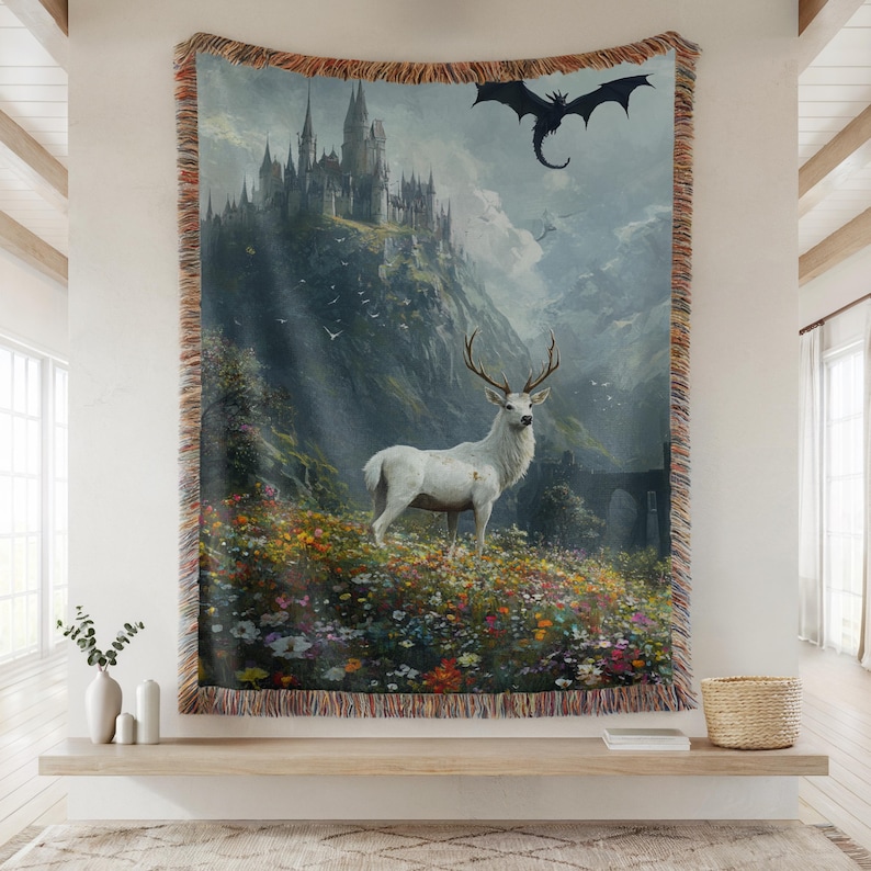 May include: A woven tapestry featuring a fantasy landscape with a white stag in a field of flowers, a castle on a mountain, and a dragon in the sky. The tapestry has a fringed border and is displayed on a wall.