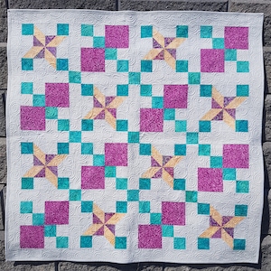 Könnte beinhalten: Eine weiße Steppdecke mit einem sich wiederholenden Muster aus rosa und türkisfarbenen Quadraten. Die Quadrate sind in einem Gittermuster angeordnet und von einem weißen Hintergrund umgeben. Die Steppdecke ist mit einem wirbelnden Muster gesteppt.