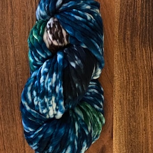 May include: A skein of blue, white and green yarn with a tie-dye pattern. The yarn is labelled "71 SNAKE ASTA SUPER BULKY - 90 yds (82 m) 4 inches - US 13-15 OR 9-10 mm"