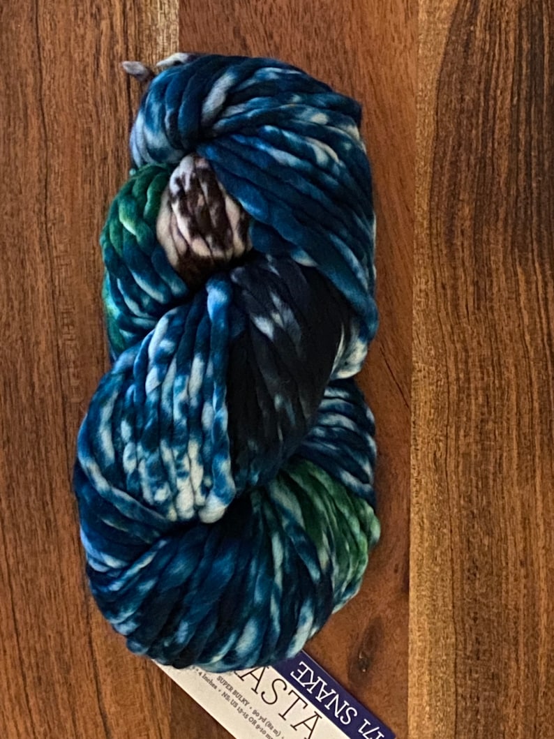 May include: A skein of blue, white and green yarn with a tie-dye pattern. The yarn is labelled "71 SNAKE ASTA SUPER BULKY - 90 yds (82 m) 4 inches - US 13-15 OR 9-10 mm"