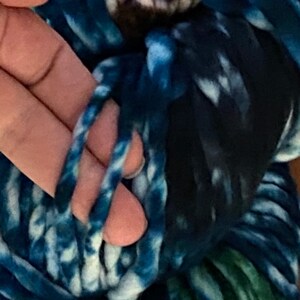 May include: A close-up of a skein of blue and white yarn with a hint of green. The yarn is soft and fluffy, and it is perfect for knitting or crocheting.