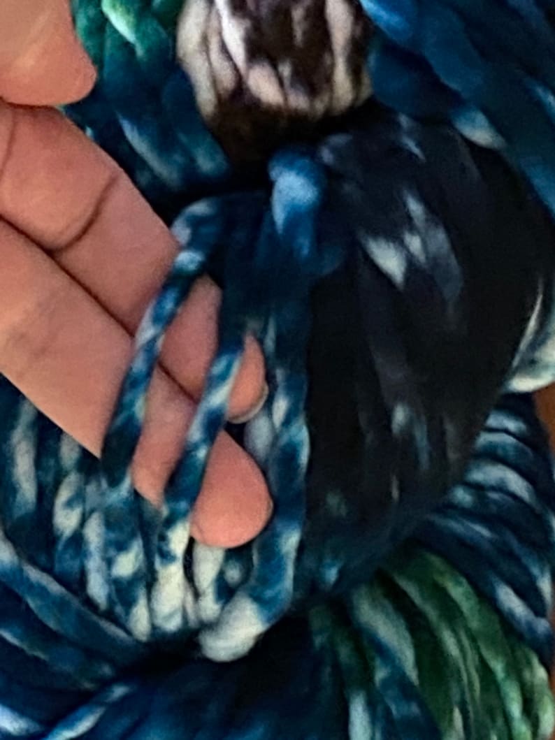 May include: A close-up of a skein of blue and white yarn with a hint of green. The yarn is soft and fluffy, and it is perfect for knitting or crocheting.
