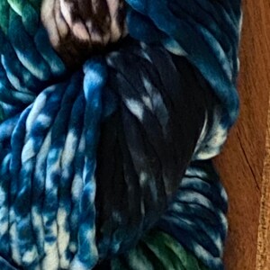 May include: A close-up of a skein of chunky yarn in shades of blue, green, and white. The yarn is hand-dyed and has a tie-dye effect.