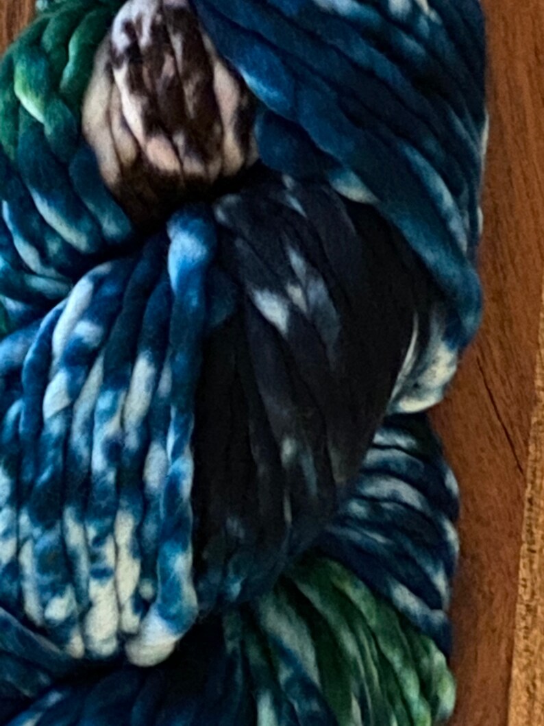 May include: A close-up of a skein of chunky yarn in shades of blue, green, and white. The yarn is hand-dyed and has a tie-dye effect.