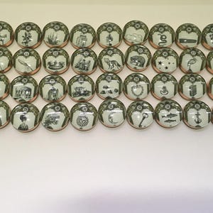 May include: A collection of thirty-six round, decorative ceramic pieces with copper-colored rims. Each piece features a unique black and white illustration, numbered 1-36, with a decorative border. The illustrations depict various scenes and objects.