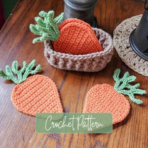 May include: A set of three orange carrot-shaped crochet coasters with green leafy tops. One coaster is stored inside a small, oval-shaped brown crochet basket, while two identical carrot coasters are placed flat on the surface nearby.