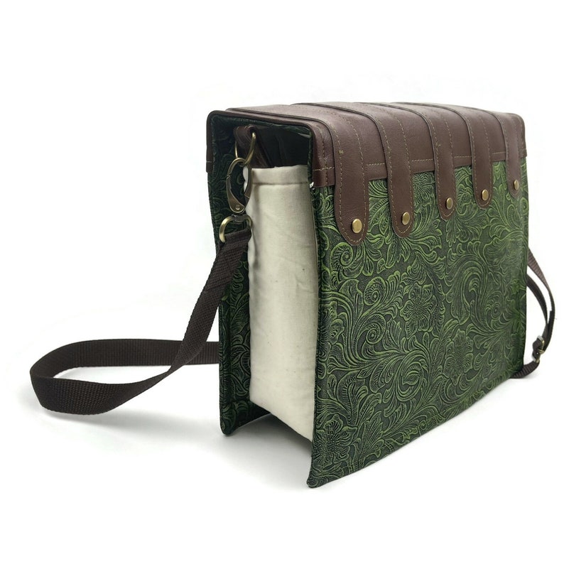 May include: A green and brown leather crossbody bag with a floral pattern. The bag has a long adjustable strap and a zipper closure.
