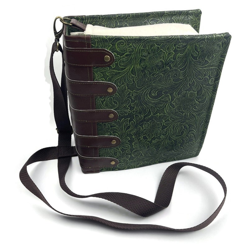 May include: A green faux leather book-style bag with a brown leather strap and metal accents. The bag has a floral embossed design and a long adjustable shoulder strap.