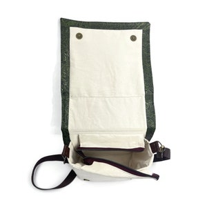 May include: A green and white patterned canvas messenger bag with a brown leather strap and a zippered pocket. The bag is open and the inside is white.