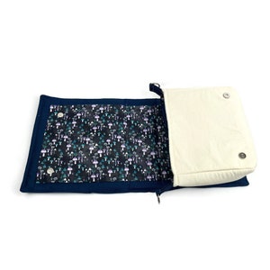 May include: A navy blue fabric bag with a zipper closure and a flap with magnetic closures. The bag is open and the inside lining is a black fabric with a white and purple mushroom pattern.