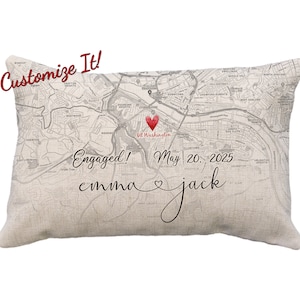 May include: A beige throw pillow with a map of a city printed on it. The map is in black and white with a red heart marking a location labeled "Mt Washington". The text "Engaged! May 20, 2025 emma jack" is printed below the map.