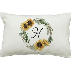 May include: A rectangular white pillow featuring a watercolor design. The design includes a wreath of sunflowers, greenery, and the letter "H" in black script. The sunflowers are yellow and brown.