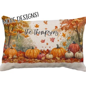 May include: Rectangular decorative pillow featuring a watercolor autumn scene with pumpkins and falling leaves. The pillow has the text "The Thompsons" and "MORE DESIGNS!" in a script font. The pillow is a fall-themed home decor item.