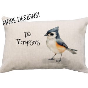 May include: A beige linen pillow with the text "The Thompsons" and a watercolor illustration of a blue and gray chickadee bird.