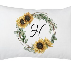 May include: White rectangular pillow with a floral design. The design features a wreath of sunflowers, greenery, and the letter "H" in black script. The sunflowers are yellow and brown.