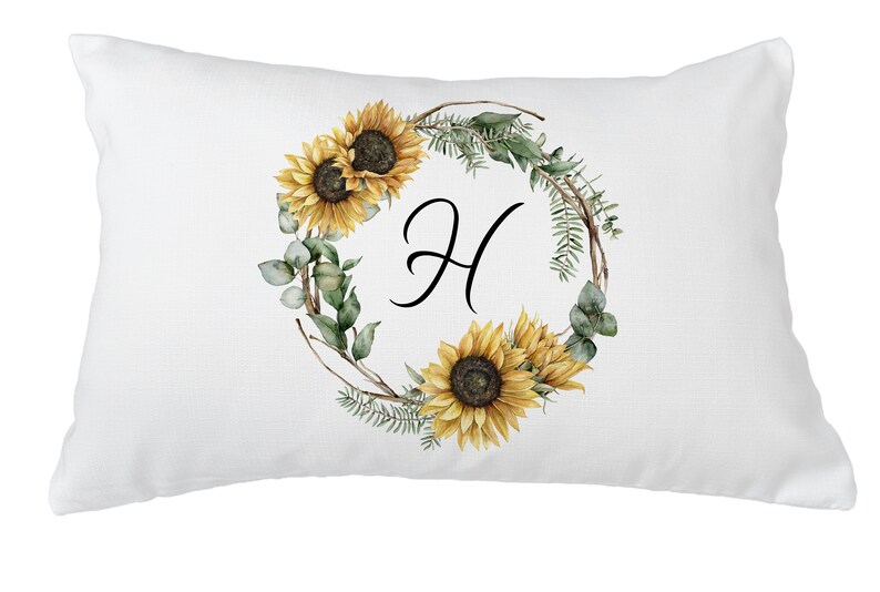 May include: White rectangular pillow with a floral design. The design features a wreath of sunflowers, greenery, and the letter "H" in black script. The sunflowers are yellow and brown.