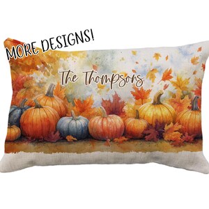 May include: Rectangular decorative pillow featuring a watercolor design of pumpkins and autumn leaves in shades of orange, yellow, and red. The text "The Thompsons" is written across the top. The pillow has a beige linen texture.