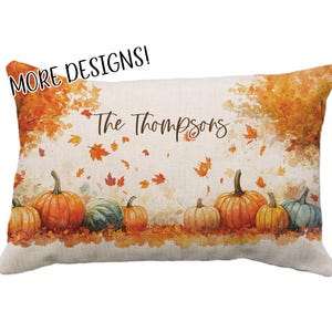 May include: Rectangular decorative pillow with a fall theme. The pillow features a watercolor design of pumpkins in shades of orange, green, and yellow, with falling leaves and the text "The Thompsons". The top left corner has the text "MORE DESIGNS!"