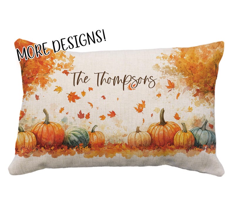 May include: Rectangular decorative pillow with a fall theme. The pillow features a watercolor design of pumpkins in shades of orange, green, and yellow, with falling leaves and the text "The Thompsons". The top left corner has the text "MORE DESIGNS!"