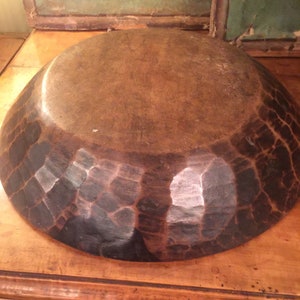 Op de afbeelding: Een grote houten kom met een donkerbruine afwerking. De kom heeft een unieke, gehammerde textuur, waardoor hij er rustiek en handgemaakt uitziet.