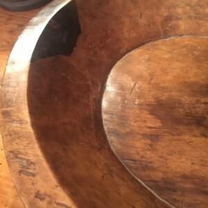 Op de afbeelding: Een grote houten kom met een donkerbruine vlek. De kom is gemaakt van natuurlijk hout en heeft een rustieke, antieke uitstraling.