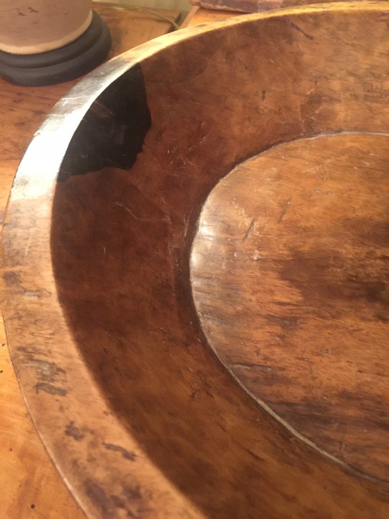 Op de afbeelding: Een grote houten kom met een donkerbruine vlek. De kom is gemaakt van natuurlijk hout en heeft een rustieke, antieke uitstraling.