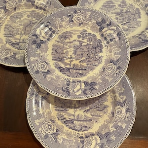 May include: Three blue and white porcelain plates with a floral pattern and a scene of a river with a mill and people in a boat. The plates have a scalloped edge.