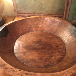 Op de afbeelding: Een grote, ronde houten kom met een donkerbruine kleur en een glad, versleten oppervlak. De kom is leeg en lijkt antiek te zijn.