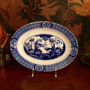 May include: A blue and white oval serving platter with a decorative border and a central design of two birds in a floral setting.