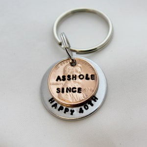 May include: A silver key chain with a penny attached. The penny has the words "ASSHOLE SINCE 1978" engraved on it. The key chain also has the words "HAPPY 40TH" engraved on it.