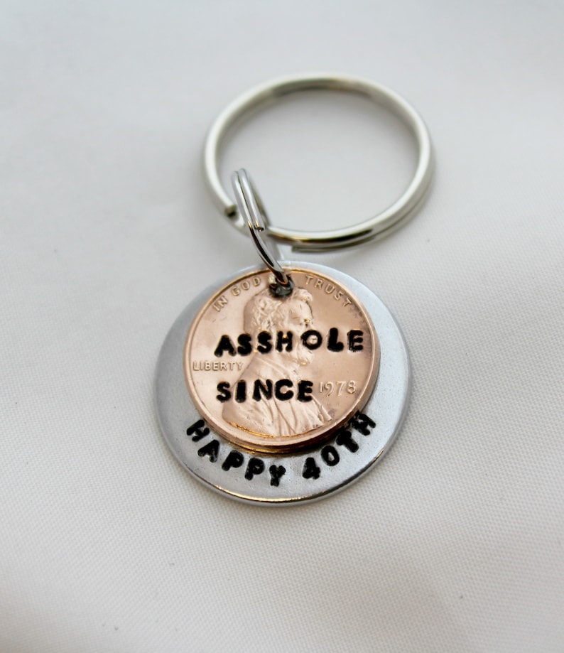 May include: A silver key chain with a penny attached. The penny has the words "ASSHOLE SINCE 1978" engraved on it. The key chain also has the words "HAPPY 40TH" engraved on it.