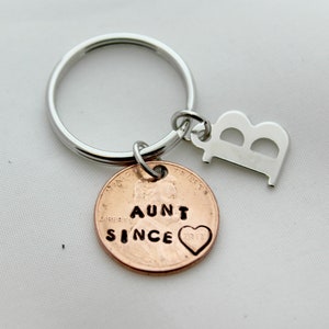 May include: A silver key chain with a copper penny charm that says "Aunt Since 2017" and a silver charm with the letter "B".