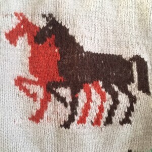 May include: A white knitted sweater with a brown and red knitted horse design.